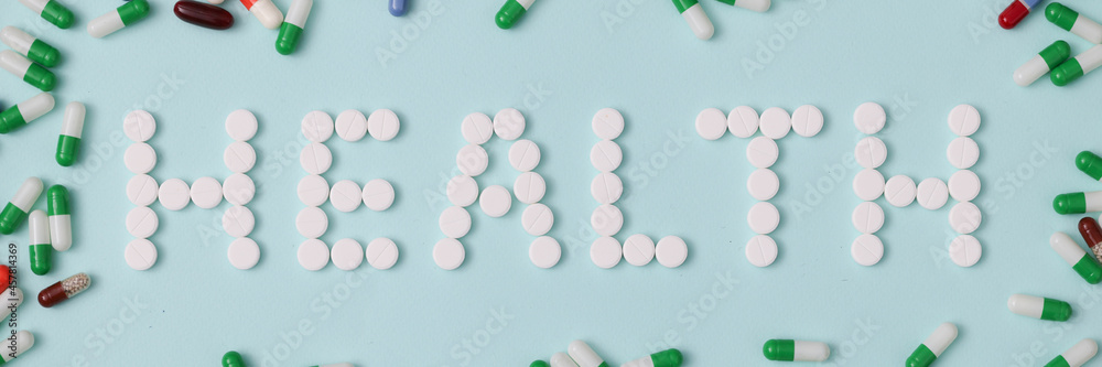 Word health is laid out from white pills on background of multicolored capsules closeup background