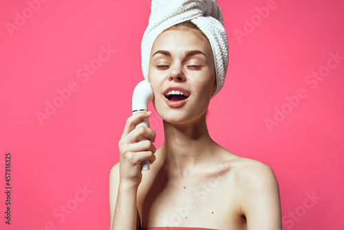 woman with towel on head cleaning face skin care pink background