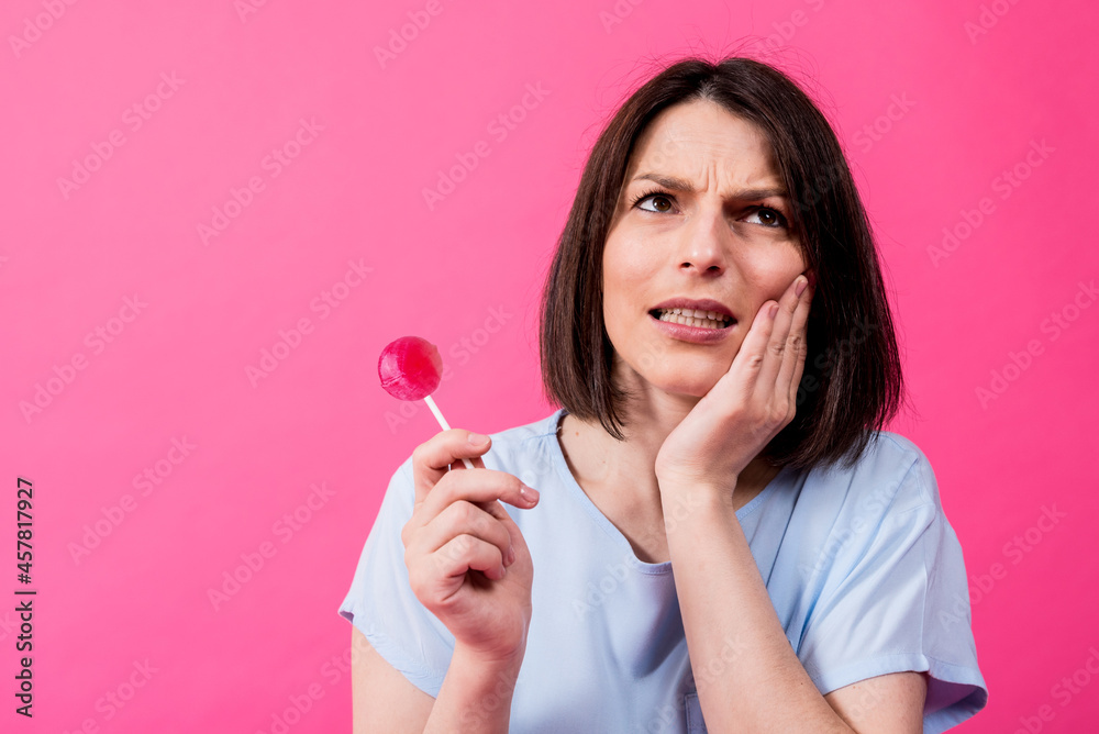 Young woman with sensitive teeth eating sweet lollipop on color background Young woman with sensitive teeth eating sweet lollipop on color background
