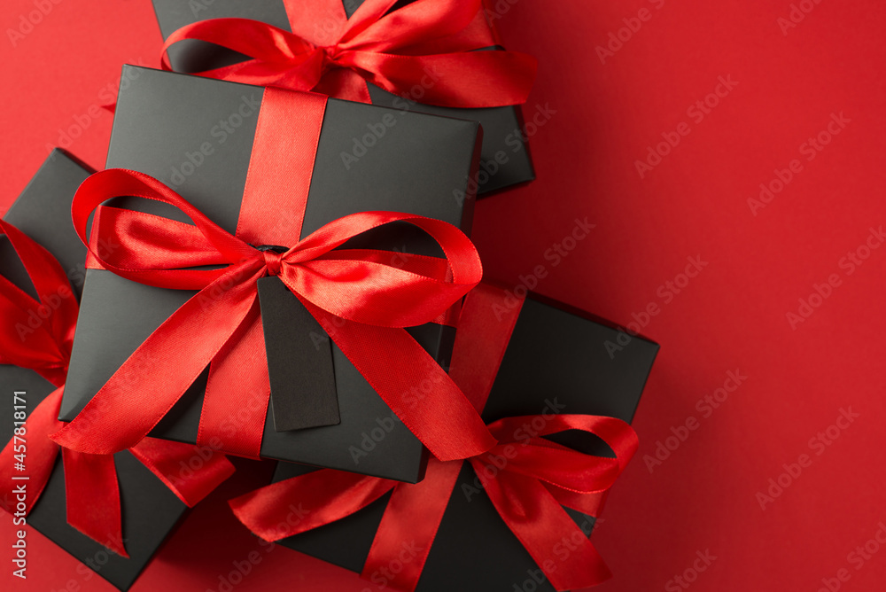 Top view photo of stack of black gift boxes with red ribbon bow and tag on isolated red background with empty space Top view photo of stack of black gift boxes with red ribbon bow and tag on isolated red background with empty space