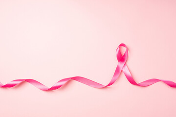 Top view photo of curly pink satin ribbon symbol of breast cancer awareness on isolated pastel pink background with empty space