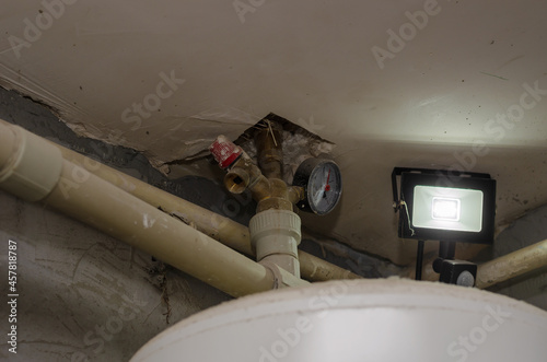Piping under the ceiling in the boiler room. Spotlight, motion sensor, pressure gauge, valve, white boiler. Inside the room. Selective focus.