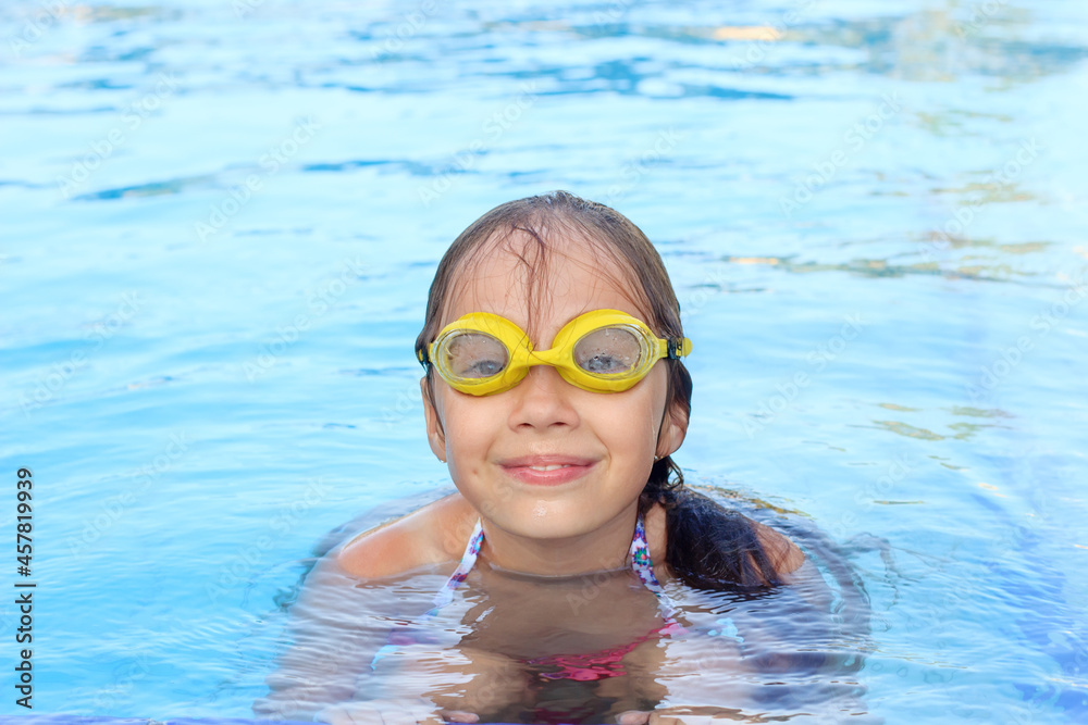 Naklejka premium Cute little girl is smiling in swimming pool. Summer, vacation, sport concept