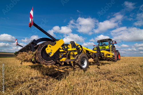tractor with a heavy disc harrow on the field with cloudly sky