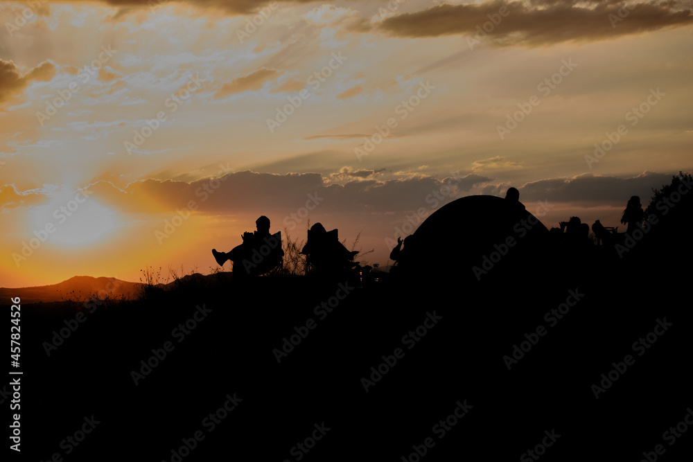 Sunset watching in rose valley sunset (kizil vadi) with silhouette of tourists and people sitting in picnic chairs and near camping tent