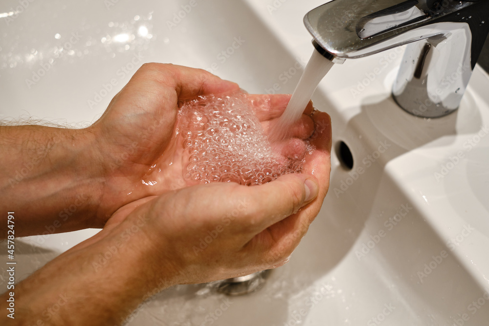 Fototapeta premium A man washes his hands with water in the bathroom. Human hands close up. Health concept. Keeping your hands clean is the best way to prevent the spread of infection
