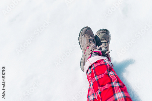 Legs in trekking shoes and red check pajama pants on the snowy ground. New year and Christmas time concept with copy space