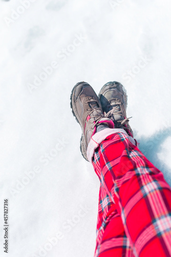 Legs in trekking shoes and red check pajama pants on the snowy ground. New year and Christmas time concept with copy space