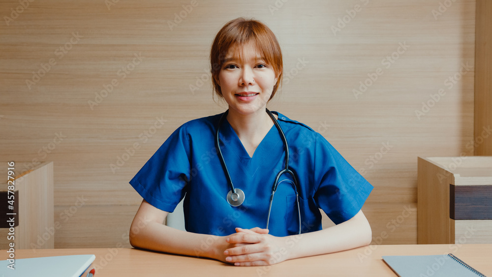 Young Asia lady doctor in white medical uniform with stethoscope using computer laptop talk video conference call with patient, looking at camera in health hospital. Consulting and therapy concept.