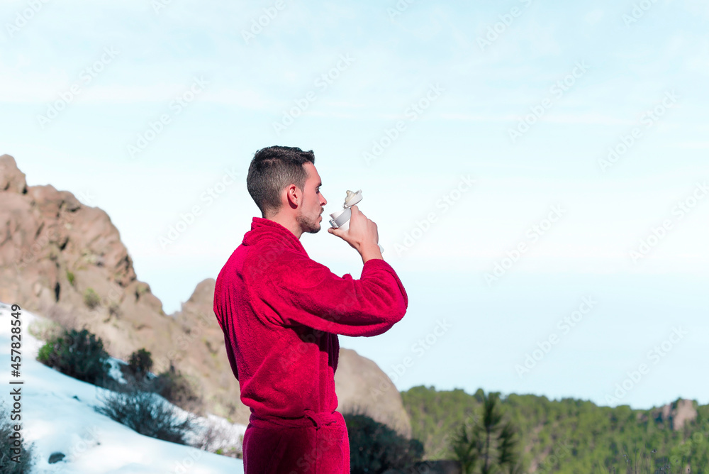 Young man in red long bathrobe is enjoying the snowy sunny day on mauntain top