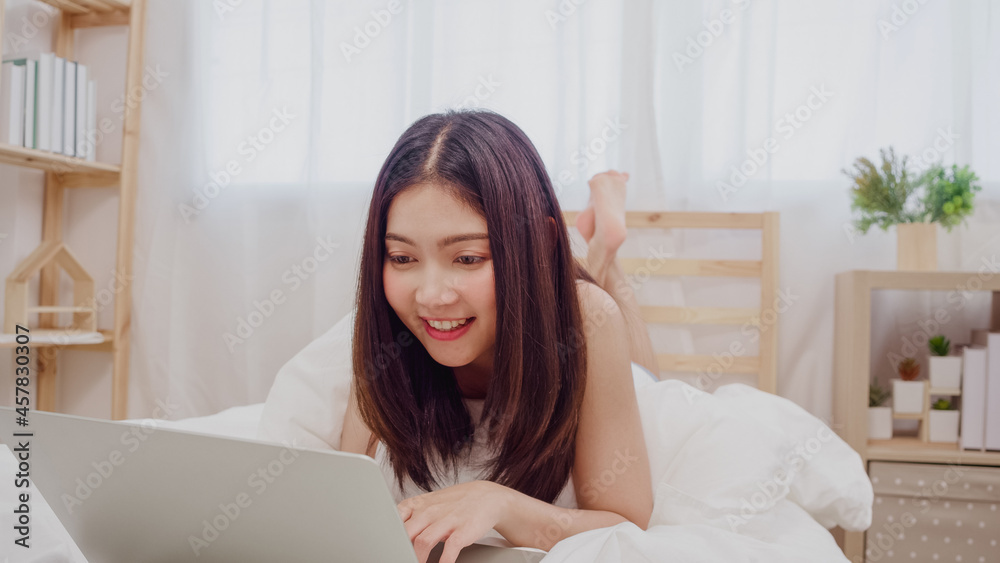 Young business freelance Asian woman working on laptop checking social media while lying on the bed when relax in bedroom at home. Lifestyle women at house concept. Young business freelance Asian woman working on laptop checking social media while lying on the bed when relax in bedroom at home. Lifestyle women at house concept.