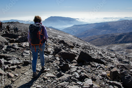 hiker descending from the top of Mulhacen with mountains and a sea of low clouds in the background photo