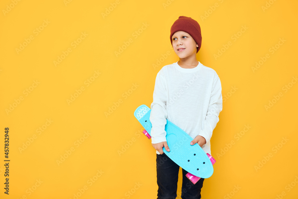 Cool smiling boy in a red hat skateboard in his hands yellow color background Cool smiling boy in a red hat skateboard in his hands yellow color background