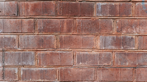 Wall of dark red rough brick close-up, textured background outside of the building outdoors, horizontal brickwork