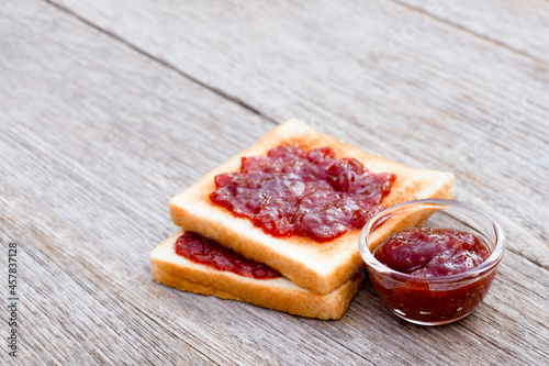 Toast sliced bread with red jam in glass bowl isolated on wooden table background. 