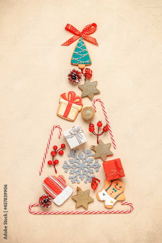 Abstract Christmas tree flat lay on beige concrete background. Christmas tree made of gingerbread, candy cane, ball, star, pine cone and gift box. Top view, vertical.