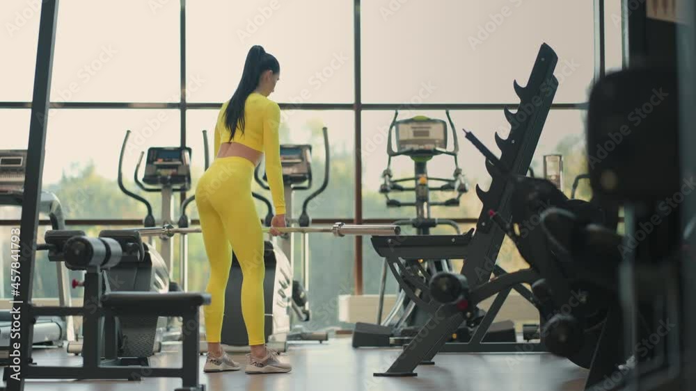 Fit hispanic woman performing weight lifting deadlift exercise with Barbell at gym In yellow sportswear. woman brunette fitness performing doing deadlift exercise with Barbell Fit hispanic woman performing weight lifting deadlift exercise with Barbell at gym In yellow sportswear. woman brunette fitness performing doing deadlift exercise with Barbell