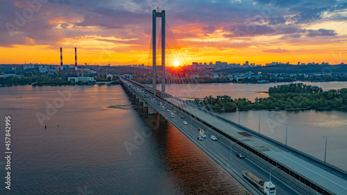 South bridge in Kiev. Sunset over the Dnieper. Thick clouds over the evening city. Evening shot of the bridge. Orange sun at sunset. The rays break through the clouds and are reflected in the river.