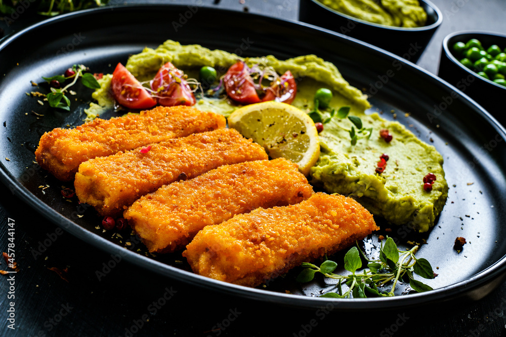 Fried fish sticks with potato and peas puree on wooden black table
Fried fish sticks with potato and peas puree on wooden black table