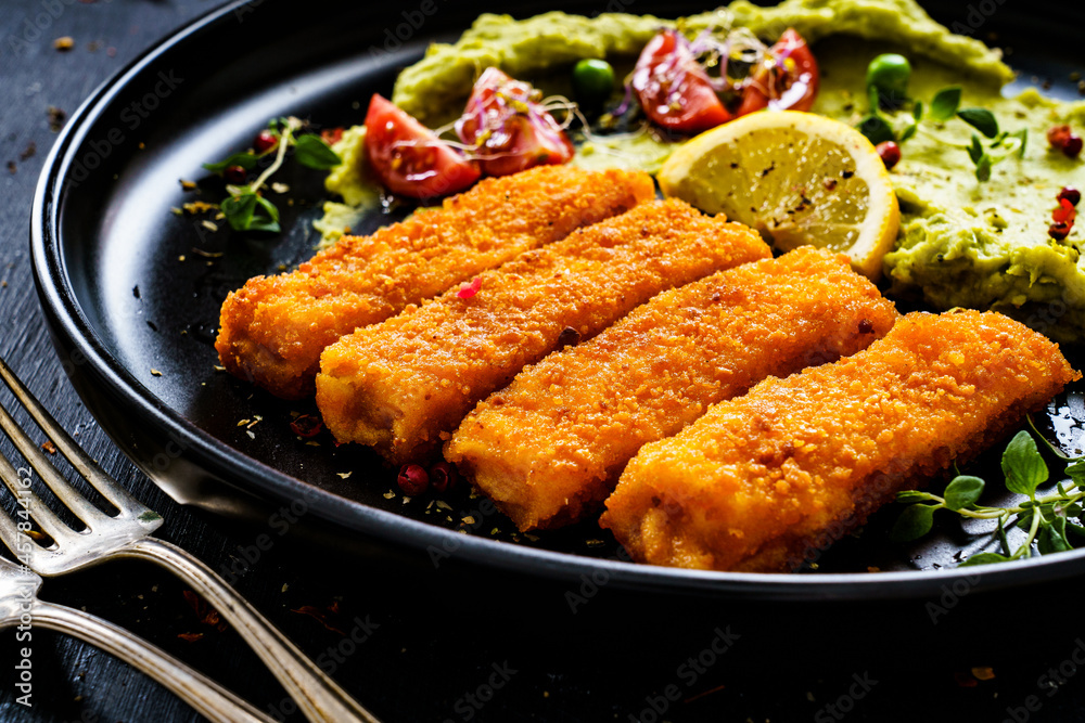 Fototapeta premium Fried fish sticks with potato and peas puree on wooden black table 