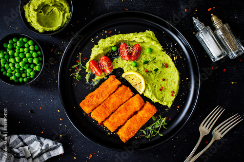 Fried fish sticks with potato and peas puree on wooden black table
 photo