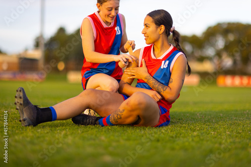 women in football uniform sitting on ground with strapping tape