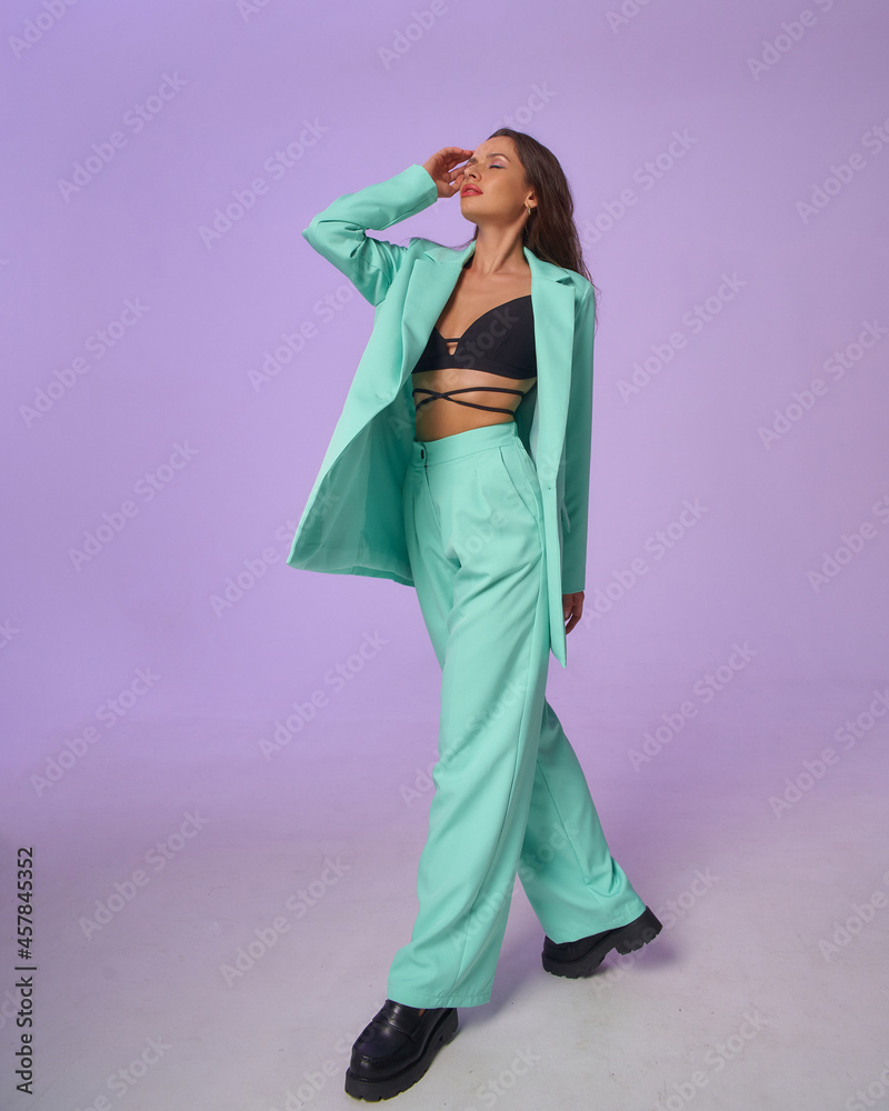 Elegant woman in mint costume blazer and pants and black top with stripes and boots standing and posing at purple background, Full length fashion portrait. Elegant woman in mint costume blazer and pants and black top with stripes and boots standing and posing at purple background, Full length fashion portrait.
