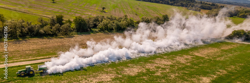 Aerial view of a tractor spreading lime on agricultural fields to improve soil quality after the autumn harvest. The use of lime powder to neutralize the acidity of the soil. Agricultural banner. © andreaobzerova