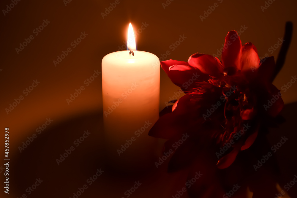 Czerwony, sztuczny kwiat i paląca się świeczka. - obrazy, fototapety, plakaty 