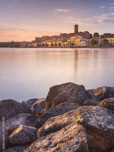 view through stones and lake to city Marta on lake Bolsena in Italy in morning lights