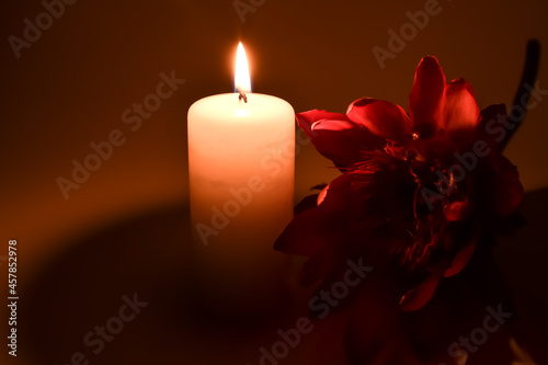 Czerwony, sztuczny kwiat i paląca się świeczka.