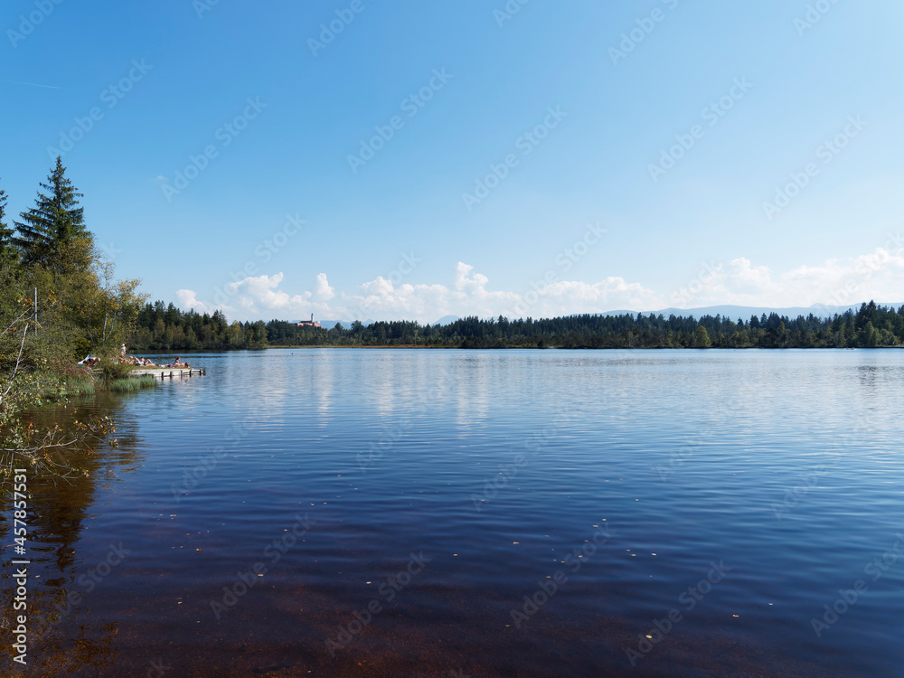 Bathing jetty and beach at Kirchsee, moor lake and popular bathing amber water by Sachsenkam in Upper Bavaria mit Blick on monastery and brewery of Kloster Reutberg