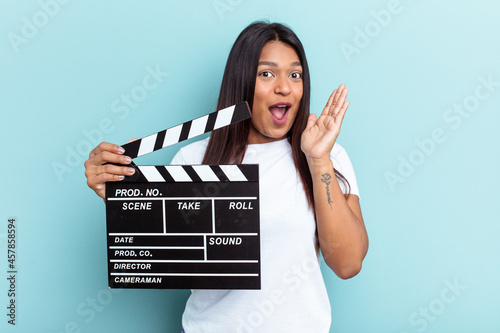 Young Venezuelan woman holding a clapperboard isolated on blue background surprised and shocked.