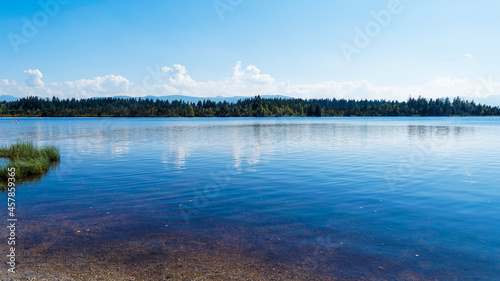 Kirchsee, moor lake by Sachsenkam in Upper Bavaria Germany with view over clean dark blue and amber water to the church of Reutberg Monastery