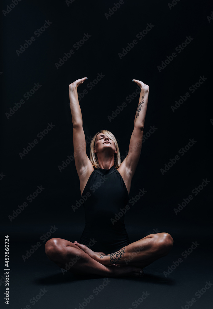 a forty-year-old woman in excellent physical shape with elastic muscles and healthy skin performs yoga exercises on a dark background. Studio photography. excellent health at forty. a forty-year-old woman in excellent physical shape with elastic muscles and healthy skin performs yoga exercises on a dark background. Studio photography. excellent health at forty.