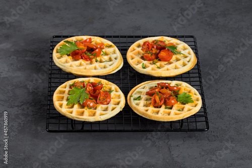 Unsweetened snack waffles with baked cherry tomatoes and parsley on a serving metal stand on a dark gray background 