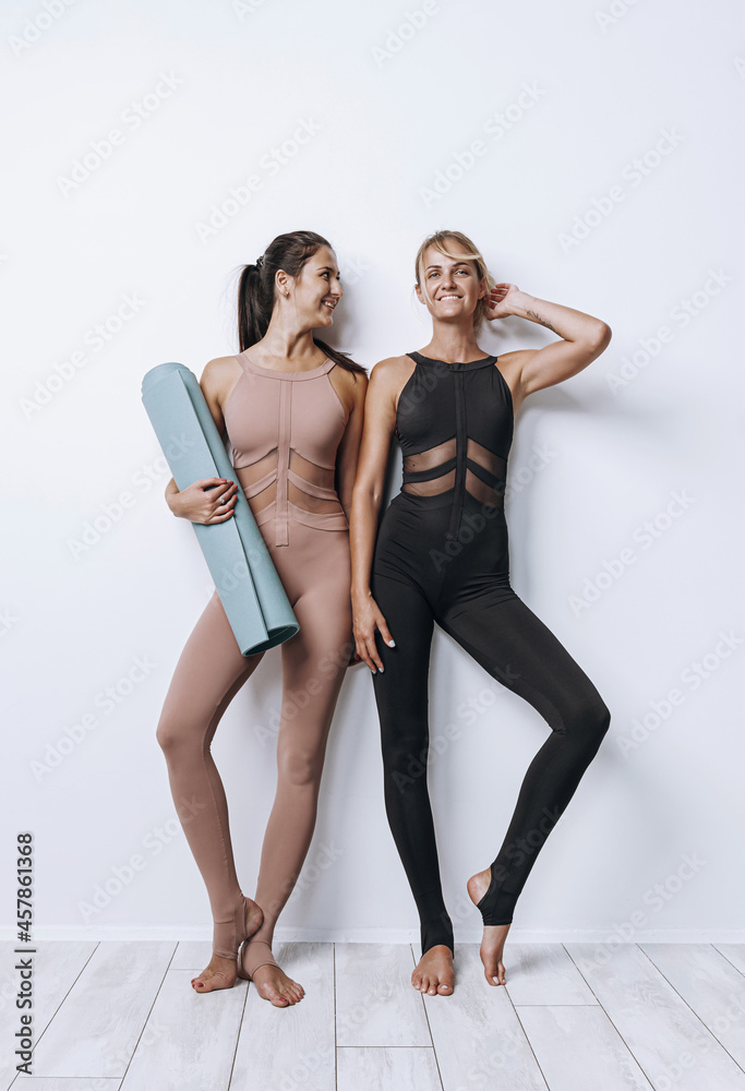 two young women in tracksuits with yoga mat on white background