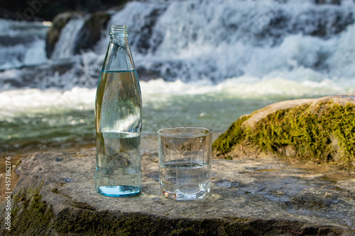 Natural drinking water in a bottle and glass beaker on nature background river