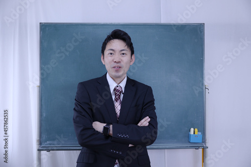 黒板の前で腕を組む日本人教師