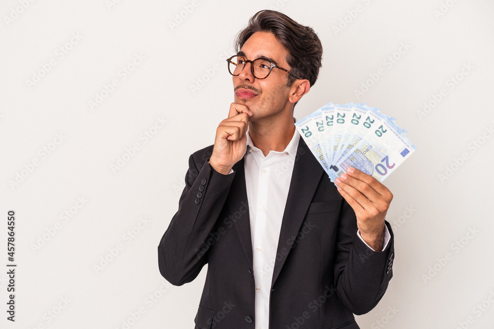 Young mixed race business man holding bills isolated on white background looking sideways with doubtful and skeptical expression. Young mixed race business man holding bills isolated on white background looking sideways with doubtful and skeptical expression.