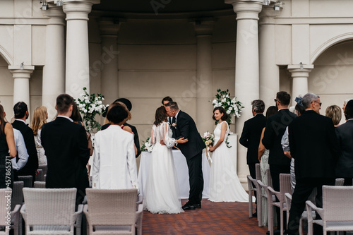 Candid shot of father walking his lesbian LGBT daughter through aisle towards her bride. Shot with 2x anamorphic lens photo