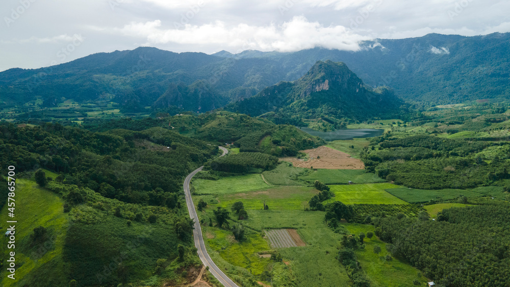 Aerial drone shot Landscape Panorama view, The roadway cuts through a fresh green forest with a car running in a mountain background.