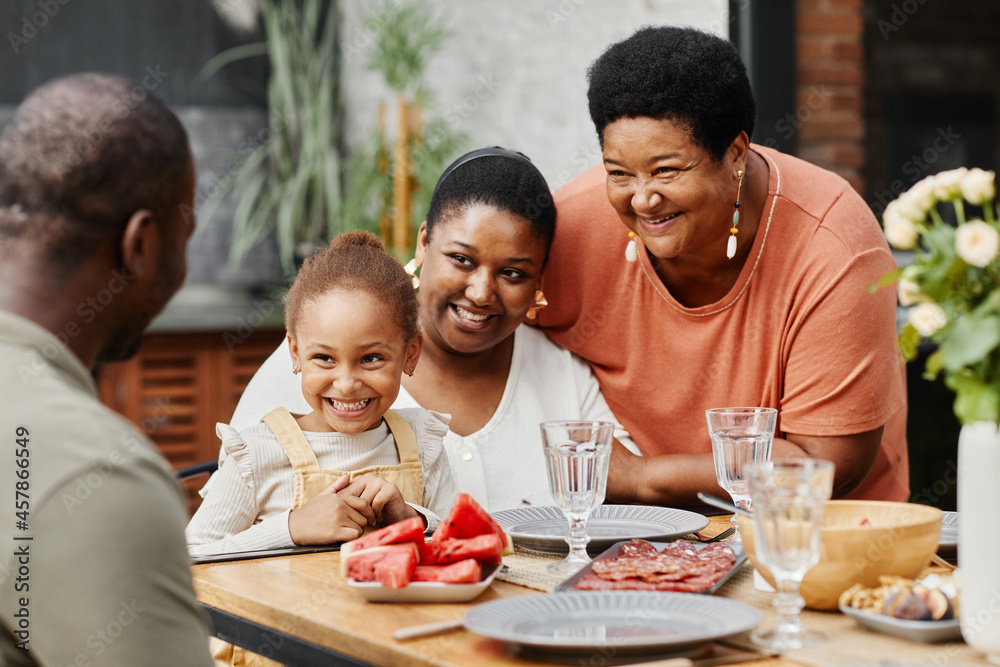Portrait of happy African-American family enjoying dinner together outdoors at terrace, copy space