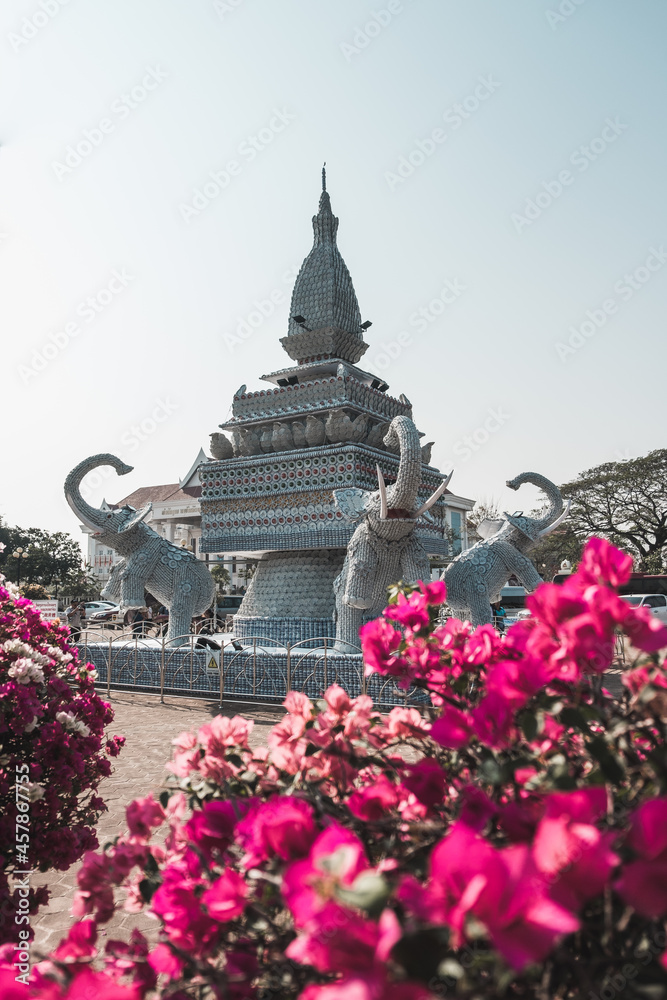 Large stone monument with elephants in the park in Vientiane in Laos. Pink flowers in the foreground