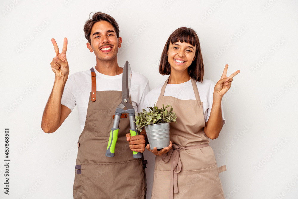 Young mixed race gardener couple isolated on white background joyful and carefree showing a peace symbol with fingers. Young mixed race gardener couple isolated on white background joyful and carefree showing a peace symbol with fingers.