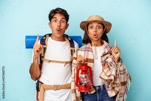 Young mixed race hiker couple isolated on blue background having some great idea, concept of creativity.