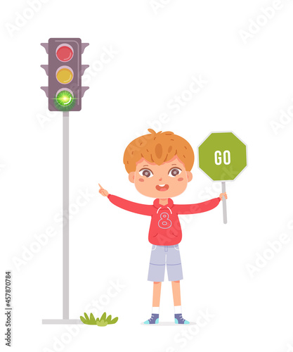 Fair-haired preschool age boy in red shirt and shorts standing at edge of carriageway on sidewalk showing on the green light, holding sign you can go