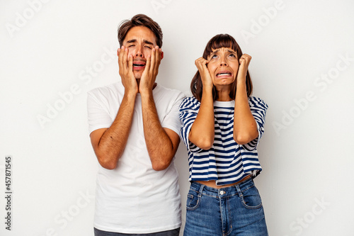 Young mixed race couple isolated on white background crying, unhappy with something, agony and confusion concept.