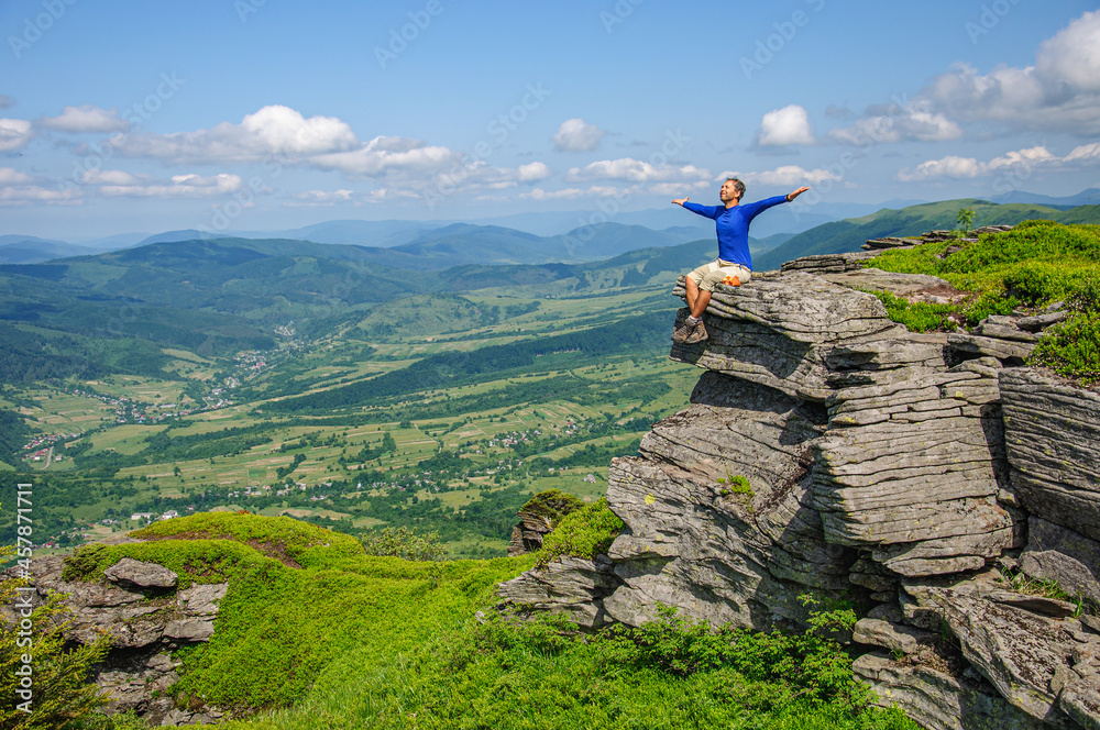 A man in a blue T-shirt sits on a high bench with his arms outstretched to the side. Ukraine Carpathians