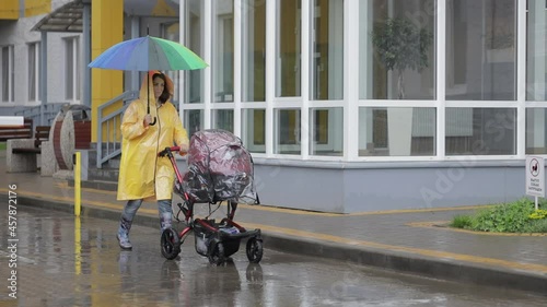 Mom with a stroller in a yellow raincoat walks in the rain